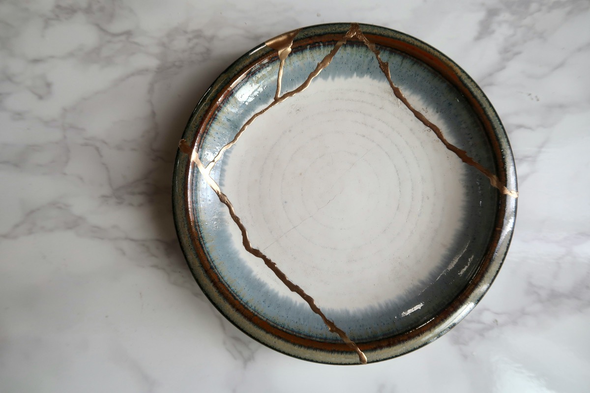 A Kintsugi ceramic bowl with gold-repaired cracks displayed on a marble surface, symbolizing trauma healing and the beauty found in brokenness